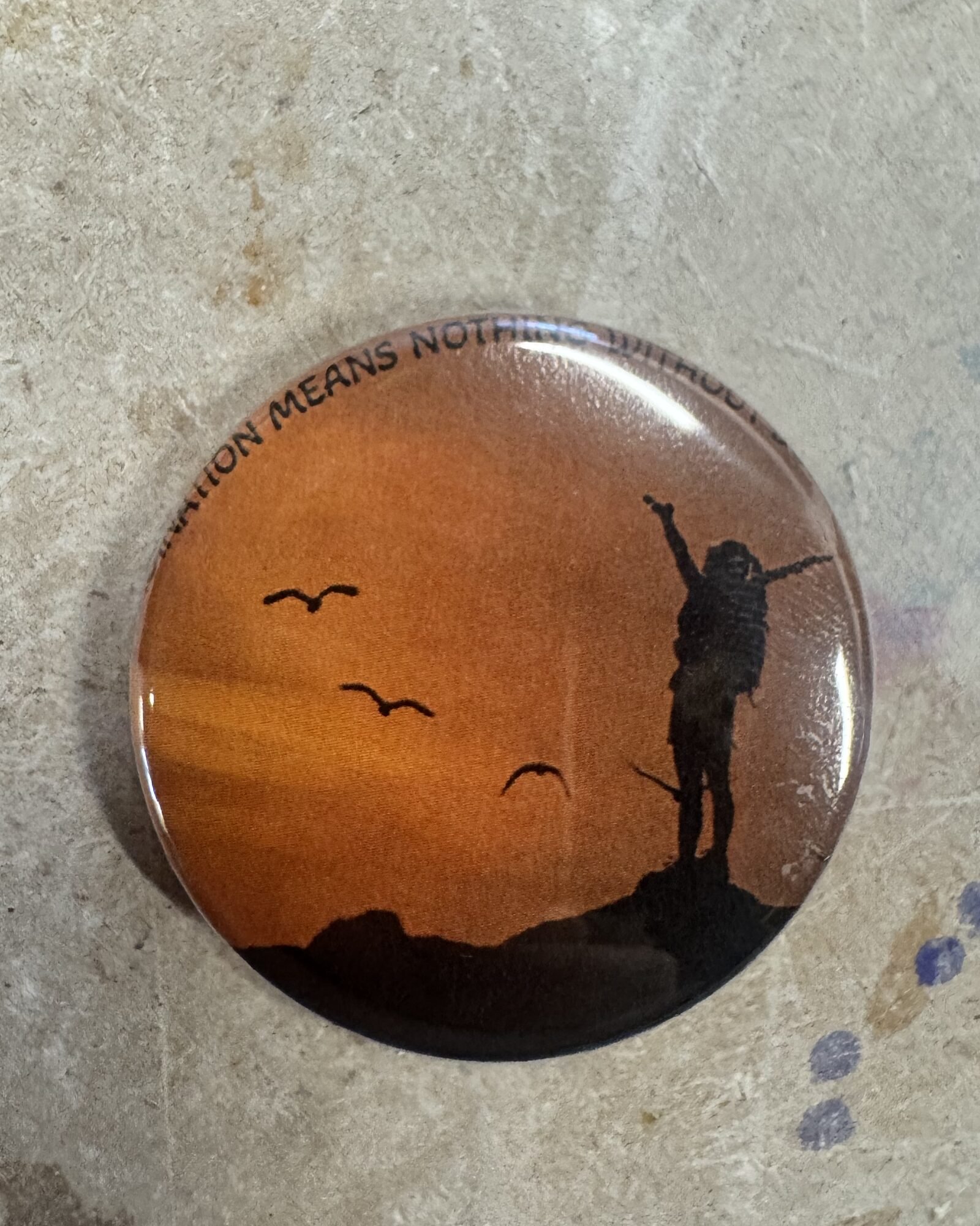 Pinback button with silhouetted figure against orange sunset