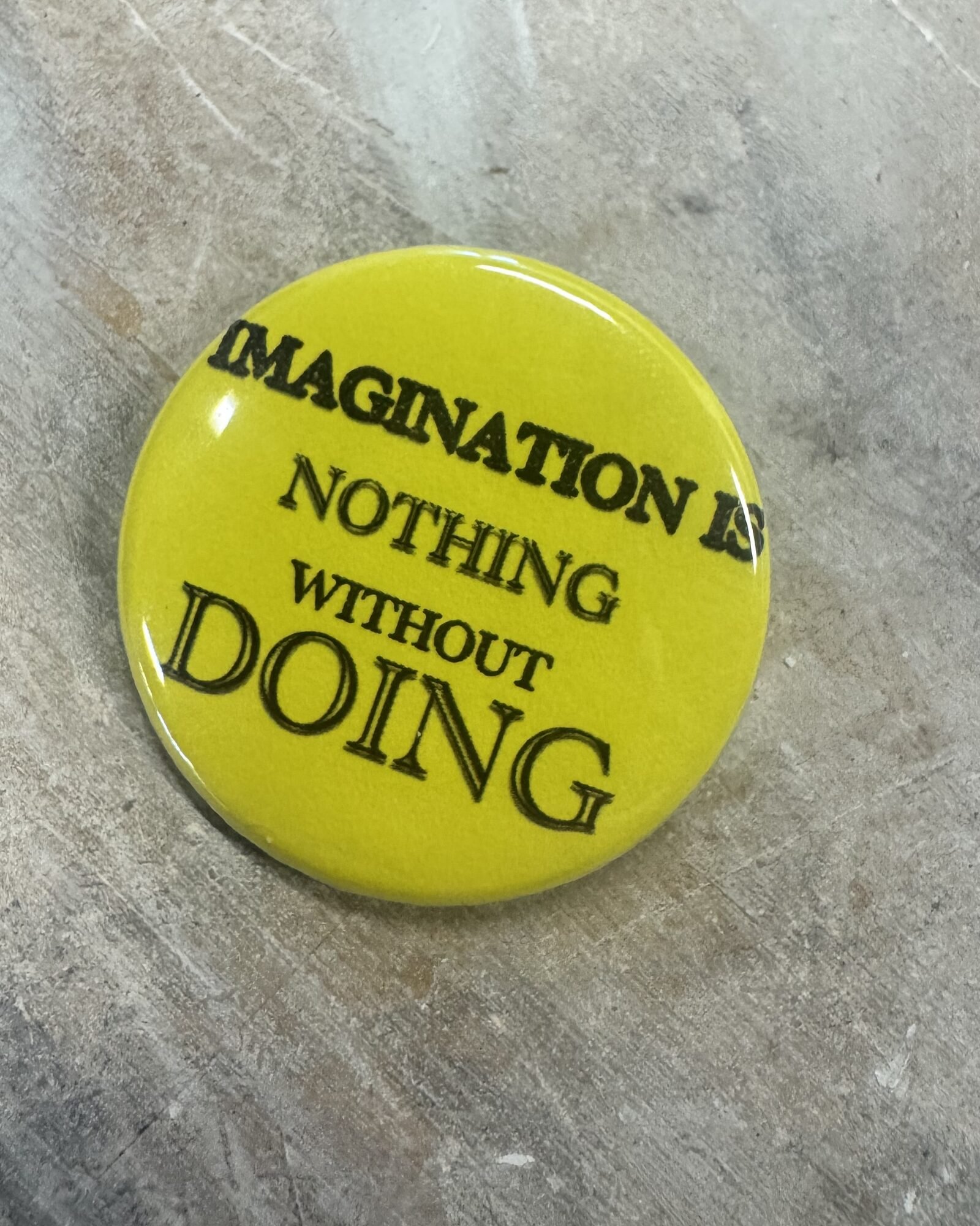 Yellow pinback button reading IMAGINATION IS NOTHING WITHOUT DOING
